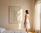 Woman in a white dress standing in a sunlit room with abstract art on the wall.
