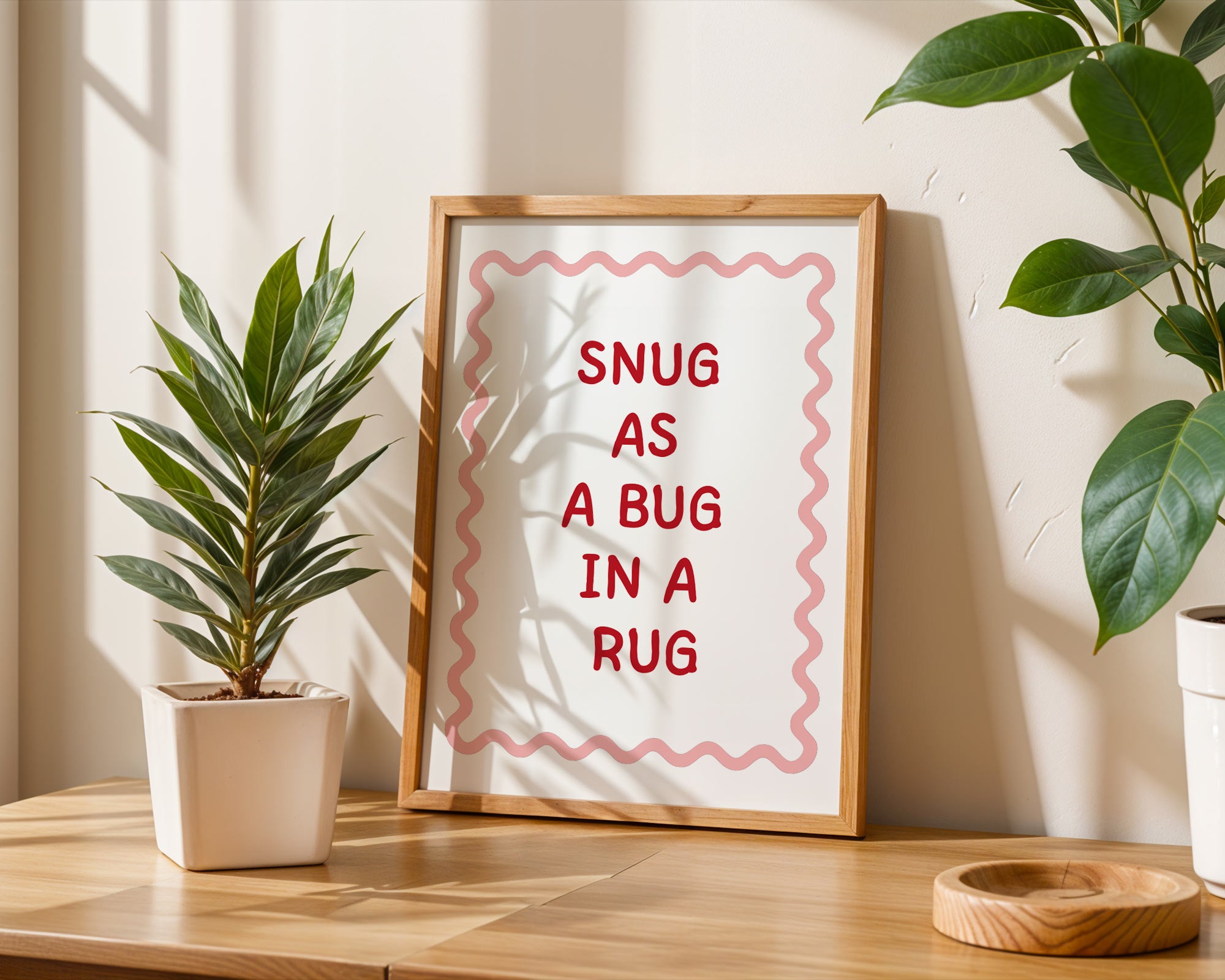 Framed print with 'Snug as a bug in a rug' text on a wooden surface with plants.