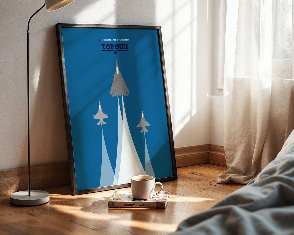 Framed 'Top Gun' poster on a wall with a cup and book on a surface below.