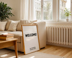 Living room with a 'WELCOME!' sign on a wooden table, books, and a plant.