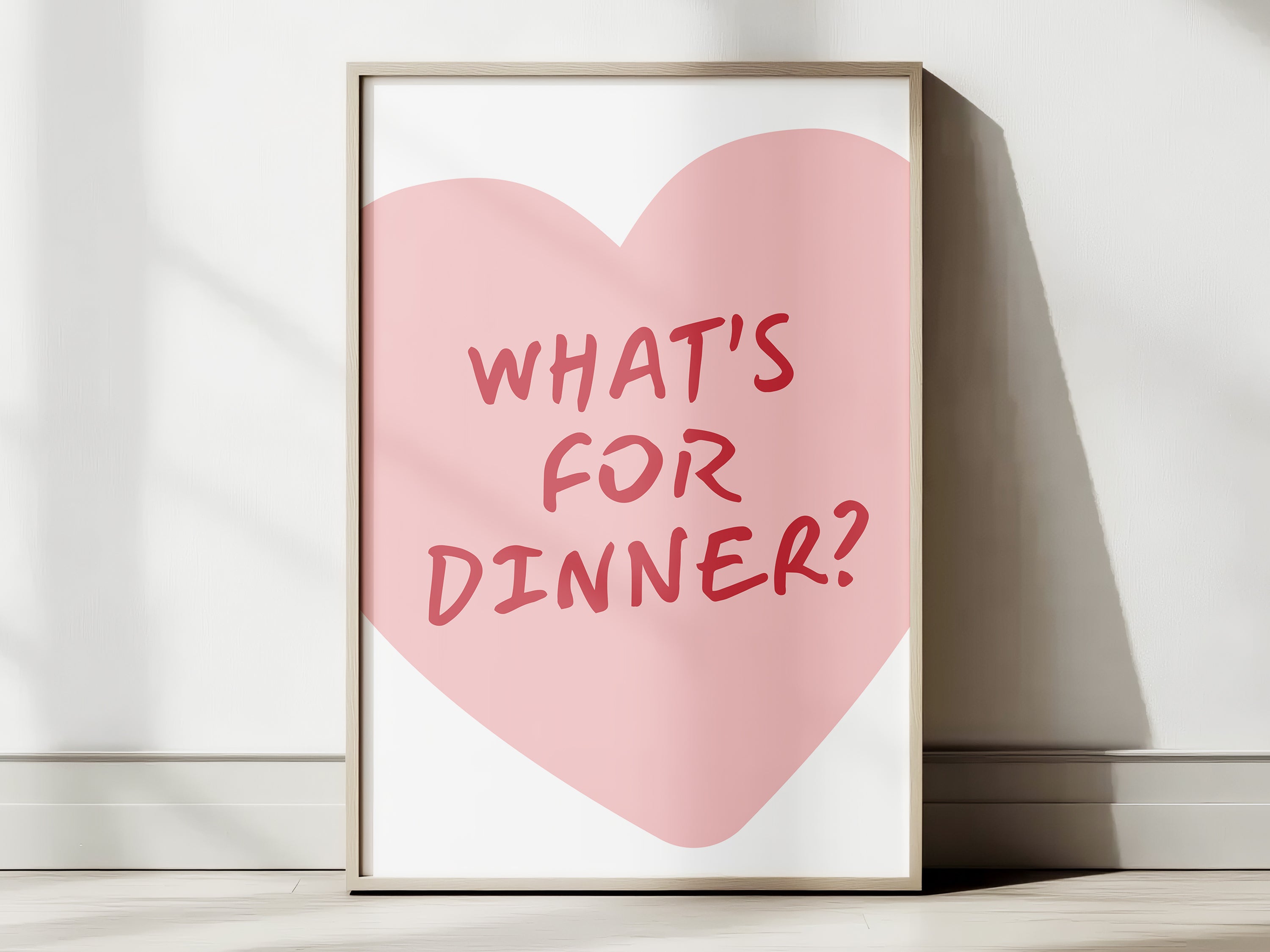 Framed print with a pink heart and 'What's for Dinner?' text on a white wall.